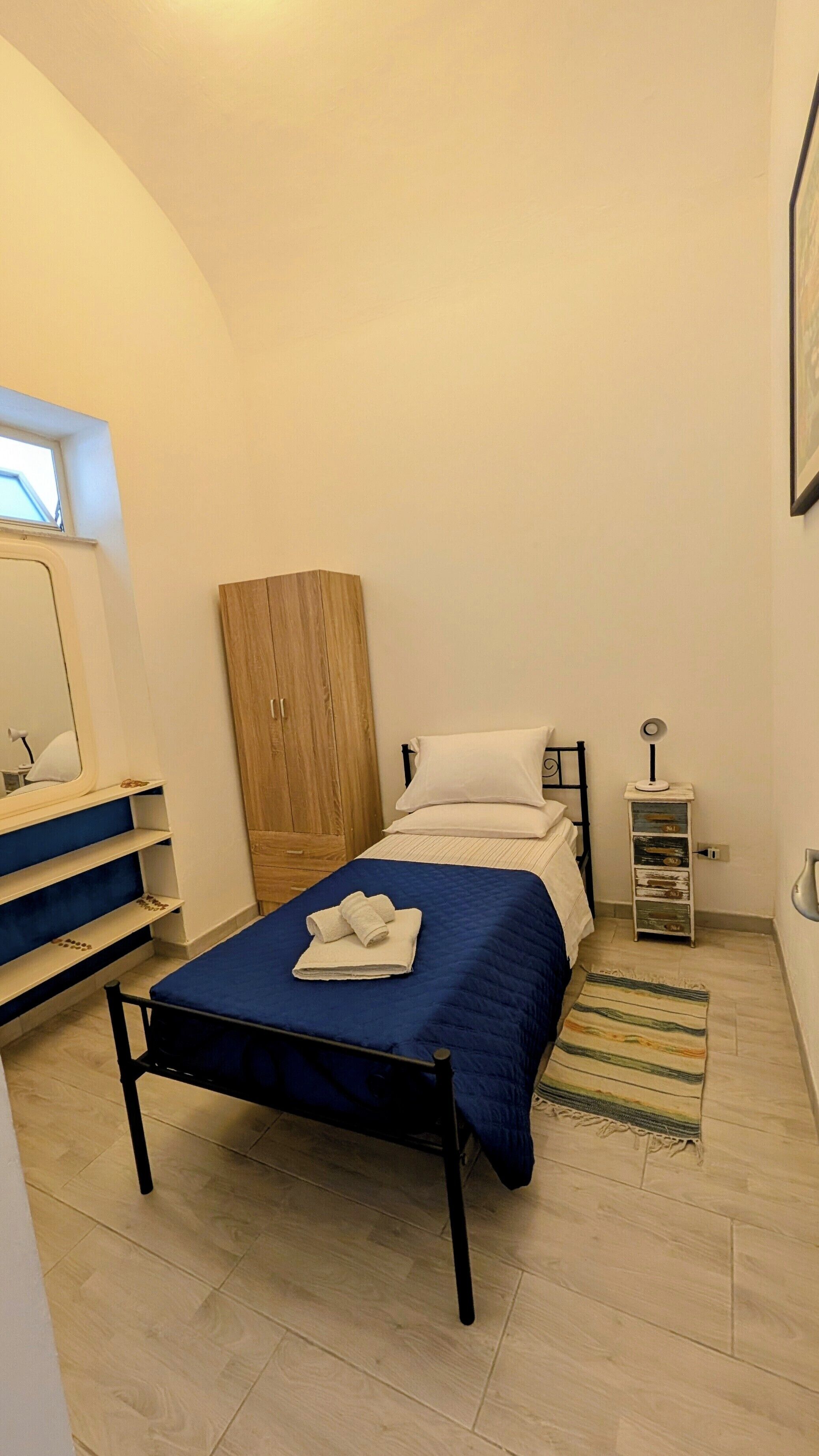 A bedroom with a bed, a wardrobe, a bedside table, a lamp, and a window.