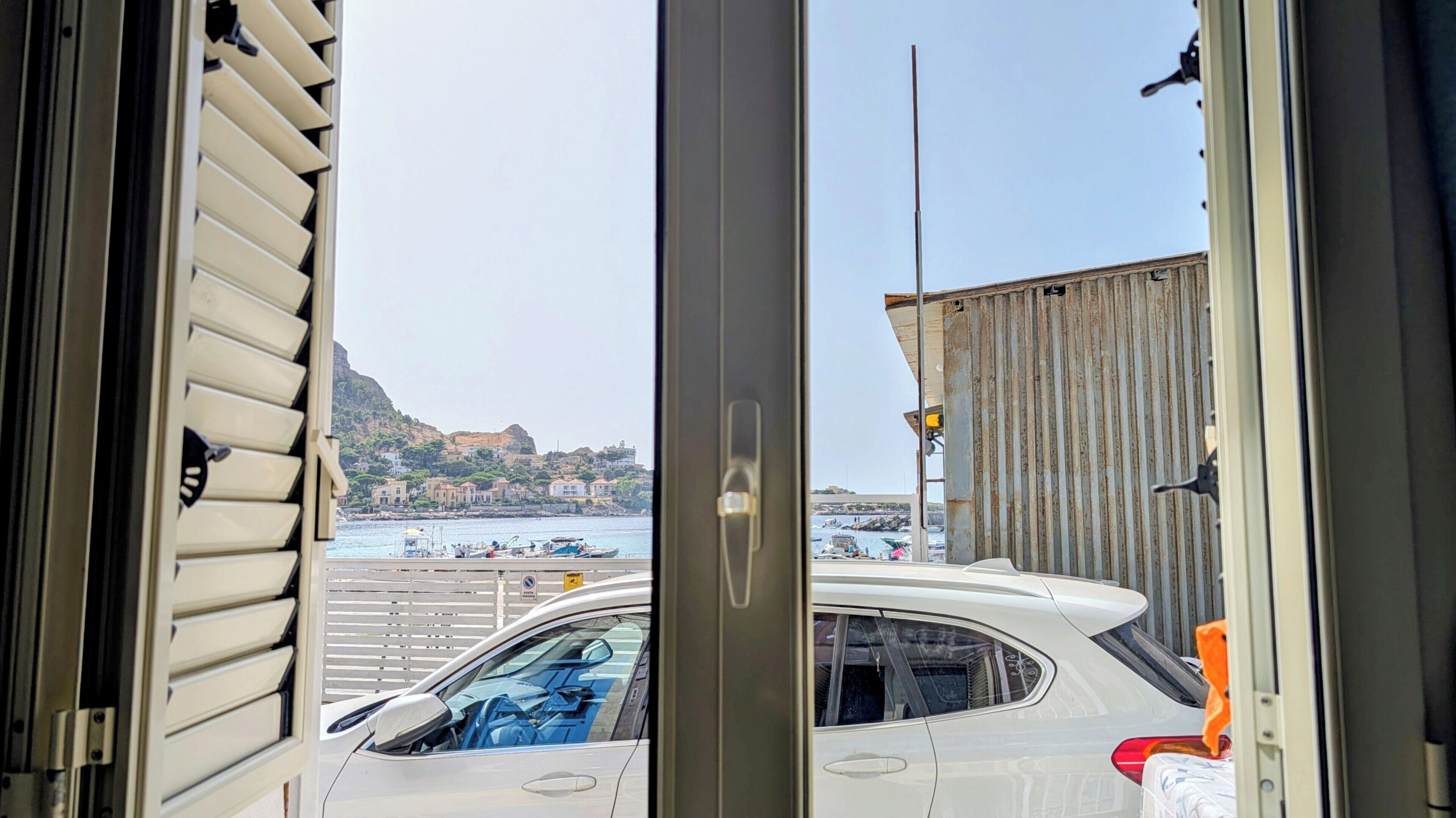 A view from inside a building looking out to a marina with boats, a coastal town, and a mountain in the distance.