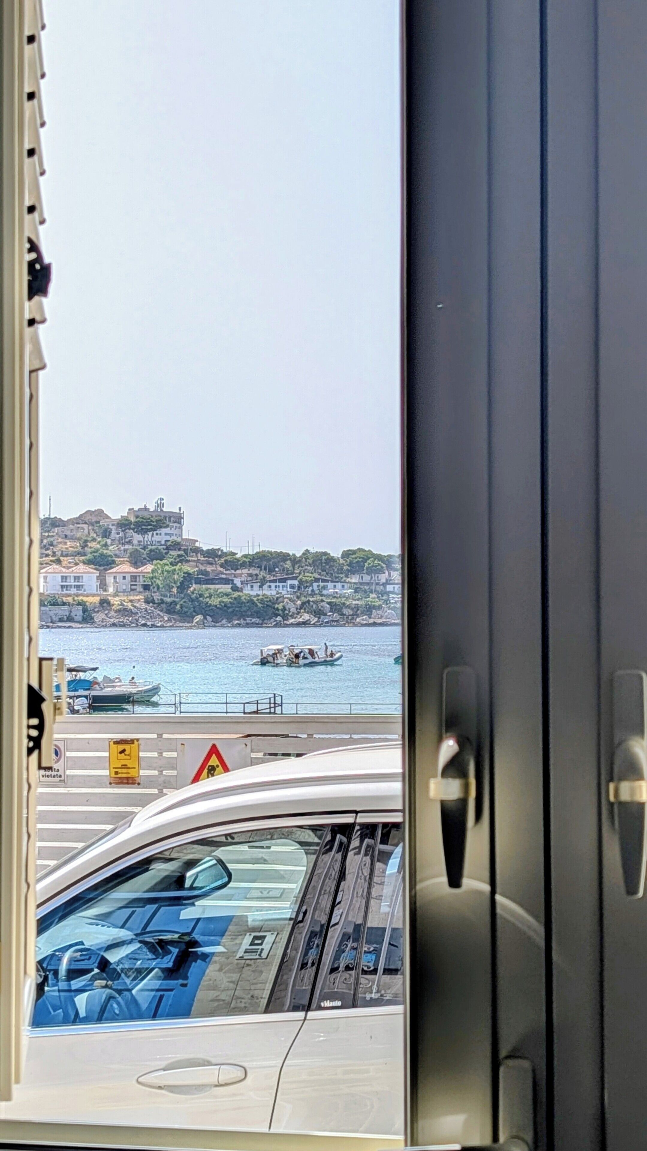 A view through a window with a coastal scene, including a body of water, boats, and buildings on a hillside.