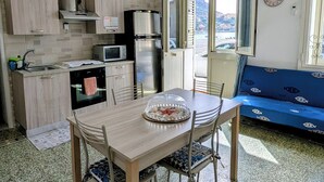 Una cuina compacta amb electrodomèstics moderns, una zona de menjador amb taula i cadires, i una vista per una porta oberta.