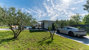 Una casa moderna con fachada blanca, un camino de entrada y un coche deportivo blanco estacionado al frente.