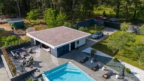Ein modernes Haus mit Swimmingpool, Sitzgelegenheiten im Freien und einem in der Nähe geparkten Auto.