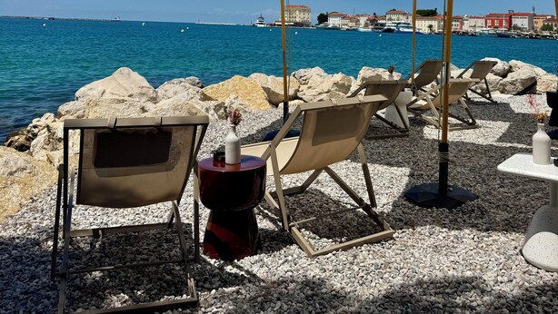 Een zitgedeelte aan het strand met parasols, stoelen en een rotsachtige kustlijn.