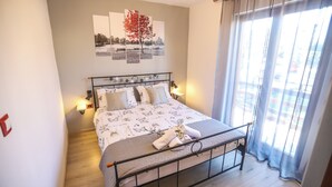 Een net opgemaakt bed met een bedovertrek met patroon, een nachtkastje met een lamp, en een wandkunstwerk erboven.