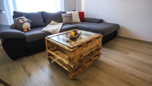Een woonkamer met een grijze bank, een houten salontafel en een zacht, pluchen uiltje.