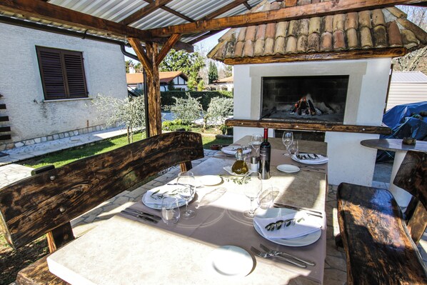 Un espace extérieur aménagé pour les repas, avec un barbecue intégré, des bancs en bois et une table en pierre, le tout prêt pour un repas.