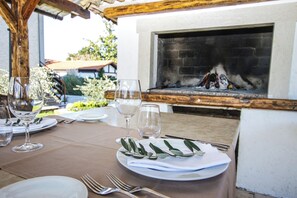 Un espace de restauration en plein air avec une cheminée en briques, des assiettes blanches, des couverts et des verres à vin vides.