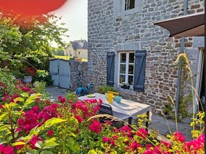 A stone building with a table and chairs outside, surrounded by vibrant flowers. - AU 15 : charming house with garden, 3 bedrooms 3 bathrooms 6 km from the beach, animals ok (Quettreville-sur-Sienne)