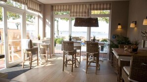 Un espace de repas lumineux et spacieux, avec des meubles en osier, de grandes fenêtres et une vue sur la mer.