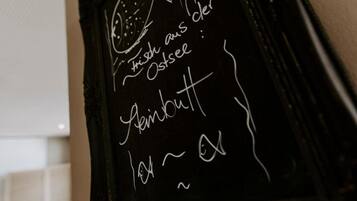 Quadro negro com texto manuscrito em língua estrangeira, possivelmente um menu ou lista.