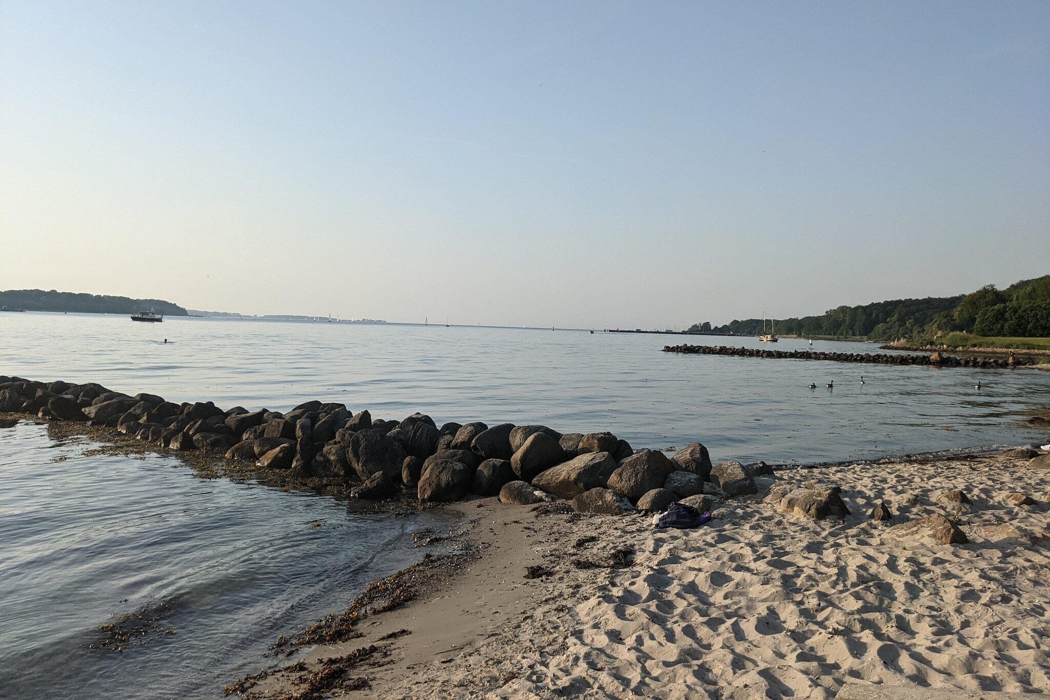 A beach with a rocky shoreline, calm water, and distant land.