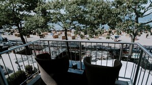 A balcony with wicker chairs and a table, overlooking a beach with sun loungers and bicycles.