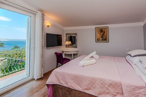 A hotel room with a bed, a desk, a chair, a TV, a painting, and a balcony with a view of the sea. - Charming Holiday Home in Maslenica (Jasenice)