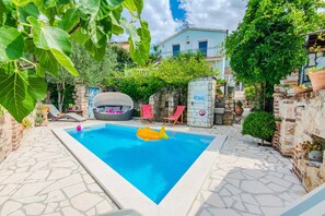 A swimming pool with a dolphin float, surrounded by stone walls and potted plants. - Charming Holiday Home in Maslenica (Jasenice)