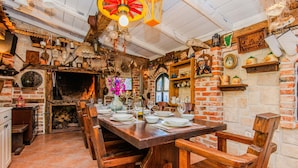 Ein rustikaler Essbereich mit Kamin aus Backsteinen, Holzmöbeln und verschiedenen Küchenutensilien, die in Regalen präsentiert werden.