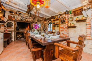 A rustic dining area with a brick fireplace, wooden furniture, and various kitchen utensils displayed on shelves. - Charming Holiday Home in Maslenica (Jasenice)