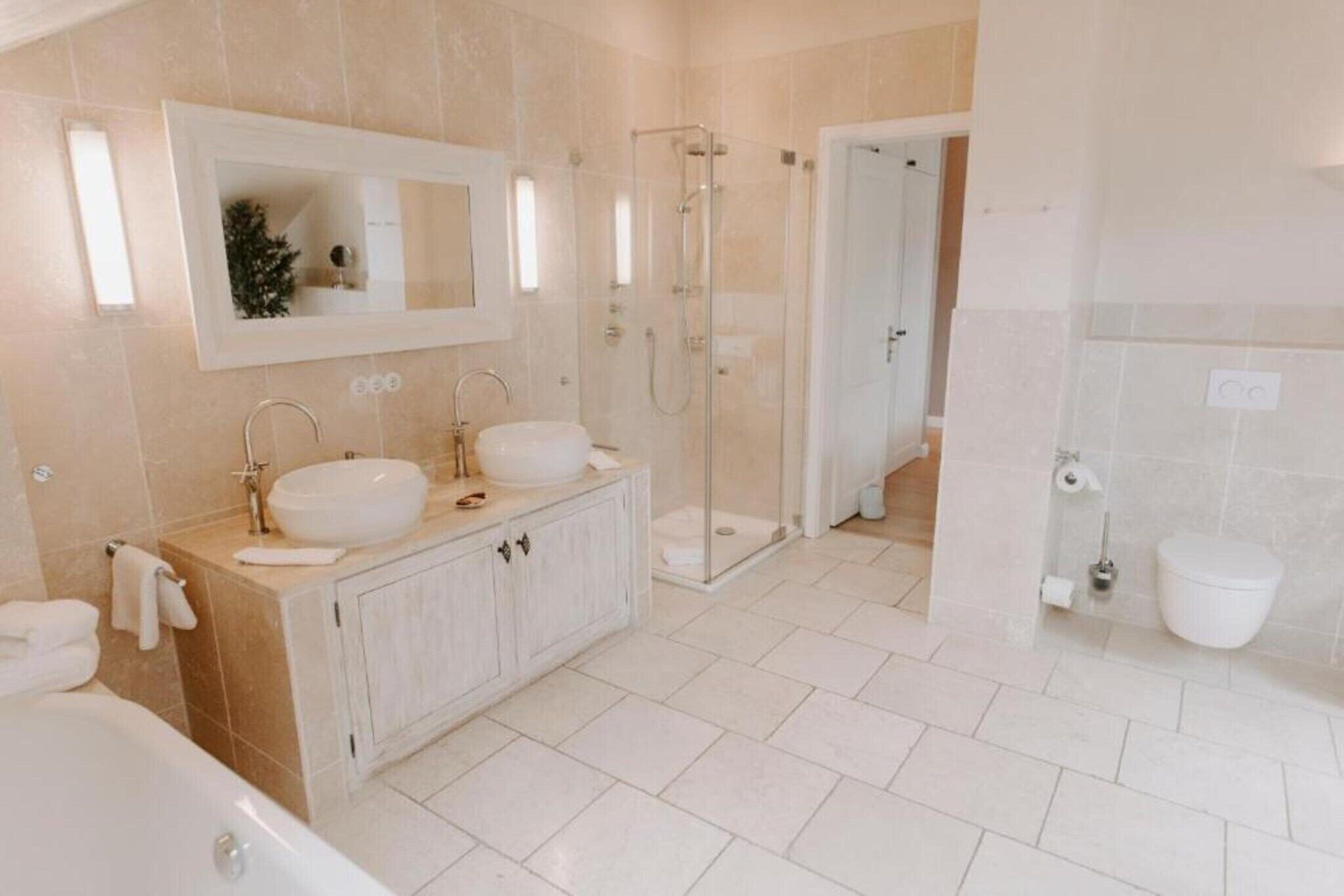 A modern bathroom with a double sink vanity, a glass-enclosed shower, and a separate toilet area.
