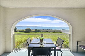 Ein Essbereich mit Tisch und Stühlen, einer Topfpflanze und Meerblick durch ein Rundbogenfenster.