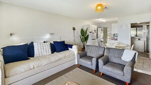 Een moderne woonkamer met een bank, twee fauteuils, een salontafel en een eethoek met een tafel en stoelen.