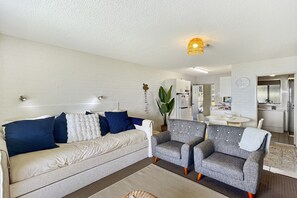 A modern living room with a sofa, two armchairs, a coffee table, and a dining area with a table and chairs. - Beachside Apartment Overlooking Casey’s Beach (Batehaven)
