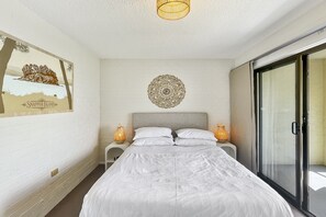 A bedroom with a bed, a wall-mounted decorative item, and a sliding glass door. - Beachside Apartment Overlooking Casey’s Beach (Batehaven)