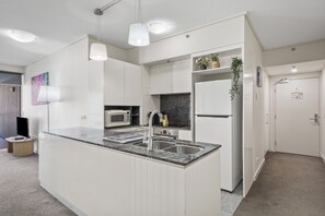 A modern kitchen with white cabinetry, a granite countertop, a built-in microwave, and a stainless steel sink. - Brisbane City Retreat with Private Balcony (Brisbane City)