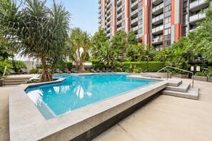 A swimming pool surrounded by lush greenery and a tall residential building in the background. - Bright 2-Bed Apartment in Bowen Hills (Bowen Hills)