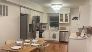 A modern kitchen with white cabinetry, a dining table set for four, and a chandelier.
