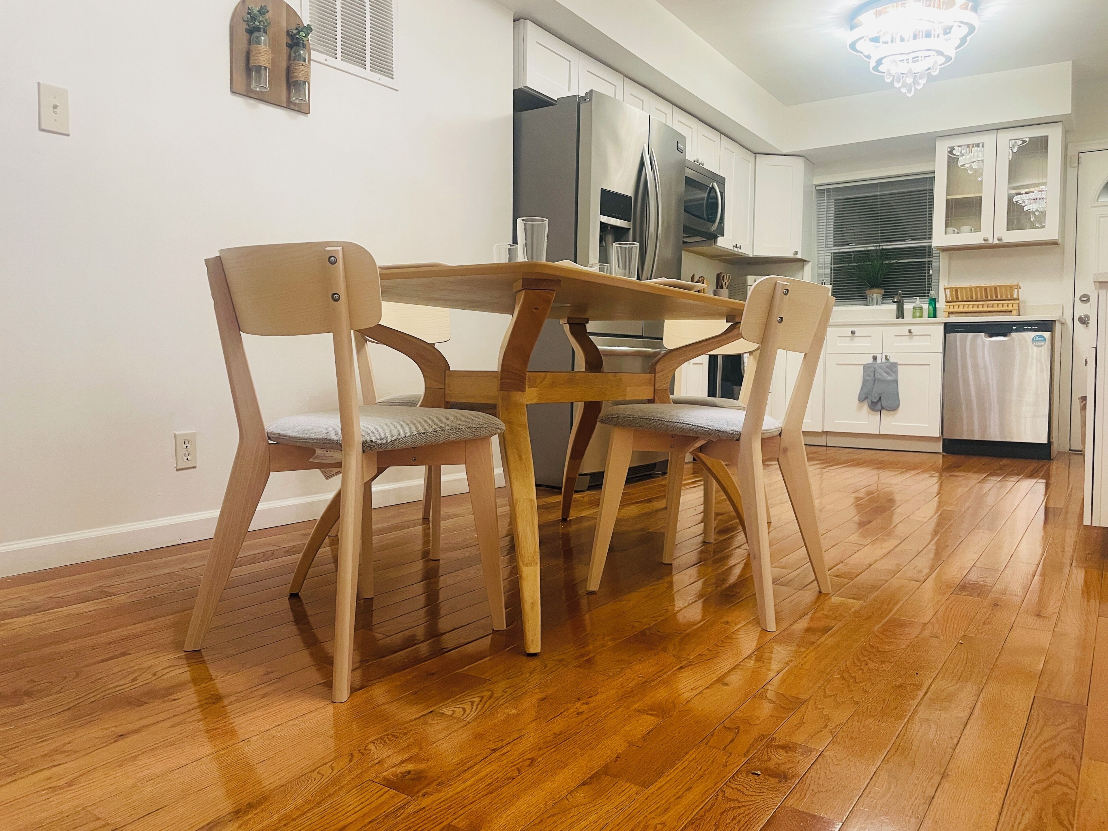 A dining area with a wooden table and chairs, a kitchen with white cabinets, and a chandelier.