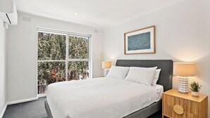 Ein modernes Schlafzimmer mit einem großen Bett, einem Nachttisch aus Holz, einer Wandleuchte und einem gerahmten Bild.