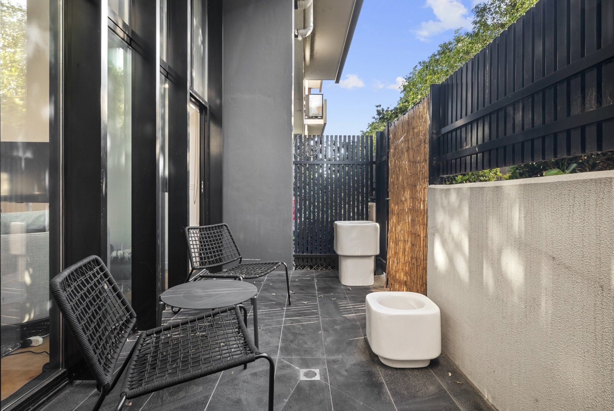 A modern outdoor seating area with two chairs and a table, a white planter, and a black fence.
