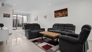 Uma sala de estar moderna com dois sofás cinzentos, uma mesa de centro de madeira e um tapete preto e vermelho.