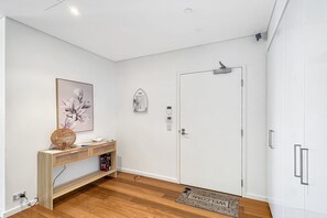 A modern, minimalist room with a wooden console table, a framed floral artwork, a white door, and a doormat. - Stylish Apartment Near Mandurah’s Best Spots (Mandurah)