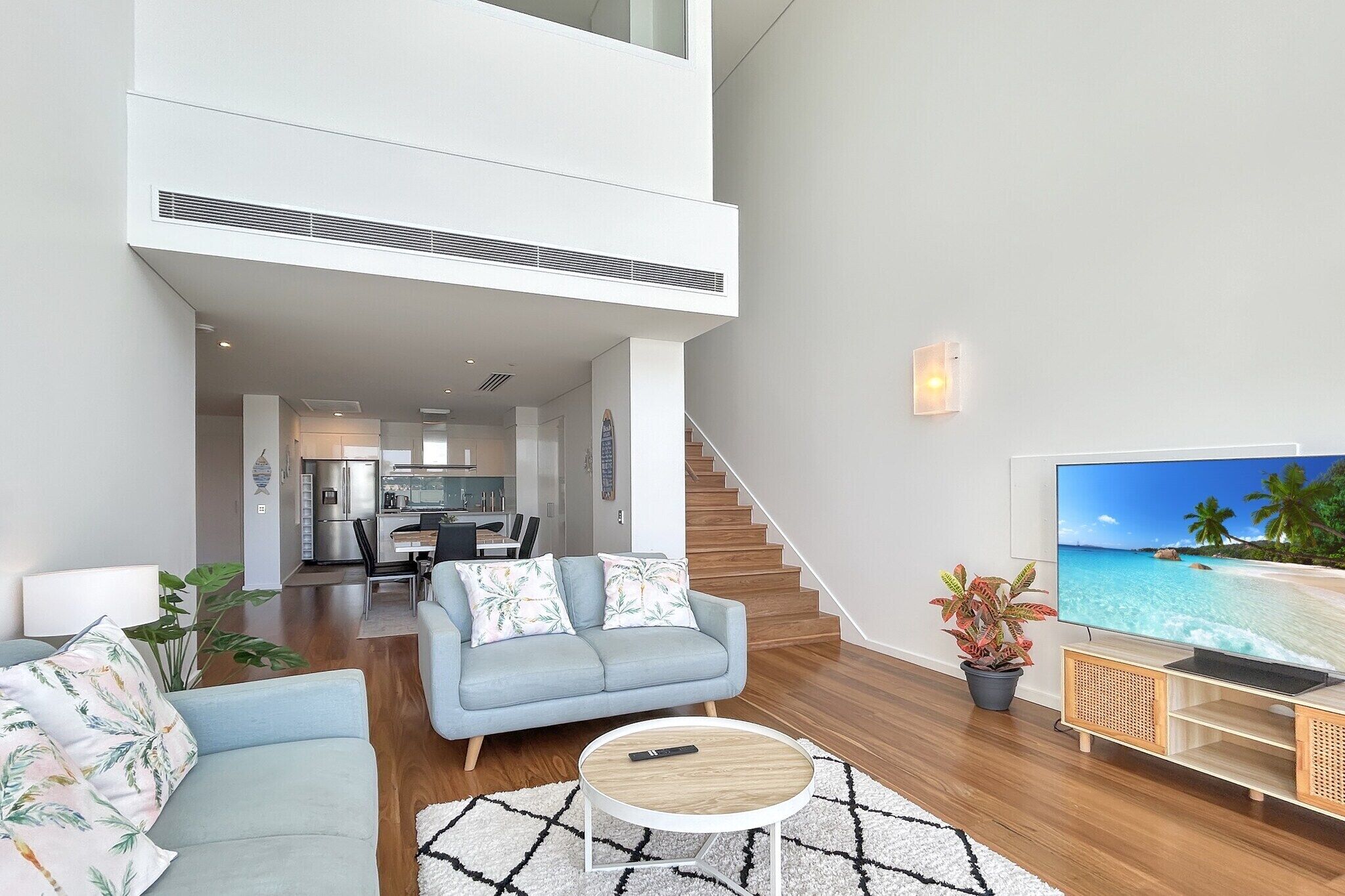 A modern living room with a sofa, coffee table, and TV. A staircase leads to an upper level.