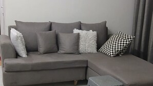 Un soggiorno moderno con un divano angolare grigio, un piccolo poggiapiedi e un tappeto bianco e nero a motivi.