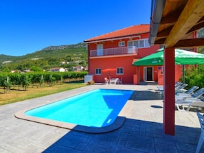 Eine rote Villa mit Swimmingpool, Außenbereich zum Sitzen und Blick auf die umliegenden Hügel.