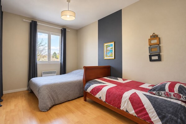 Ein Schlafzimmer mit zwei Betten, einem Vorhangfenster, einer Deckenleuchte und Bilderrahmen an der Wand.
