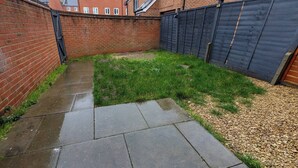 A brick wall, a concrete pathway, and a grassy area with a wooden fence. - Charming 5-bedroom Townhouse in Central Gloucester (Gloucester)
