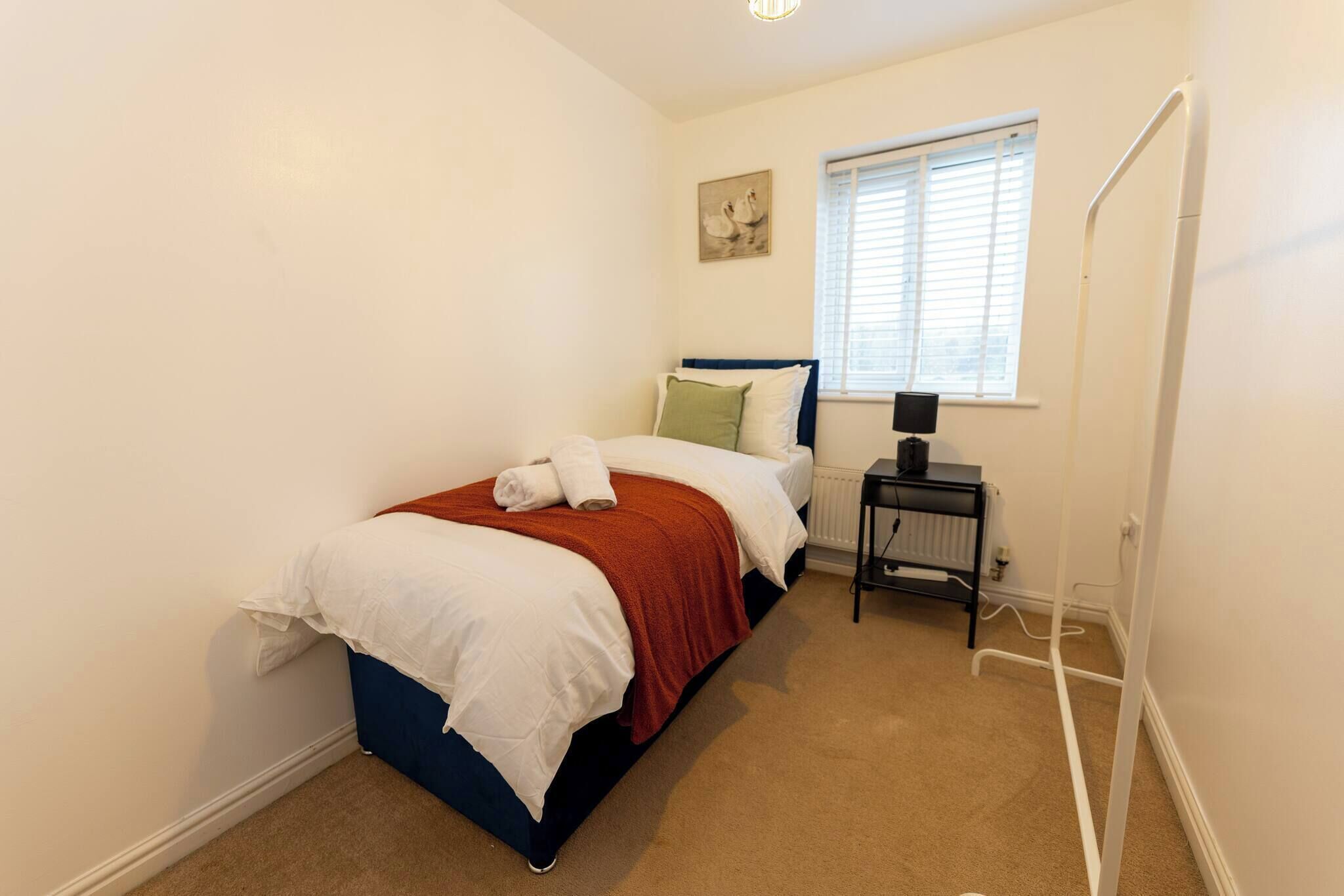 A bedroom with a bed, a nightstand, a radiator, and a window with blinds.