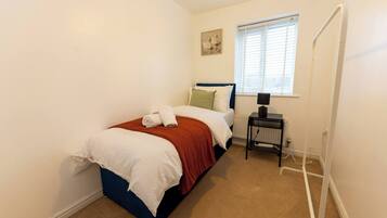 A bedroom with a bed, a nightstand, a radiator, and a window with blinds.
