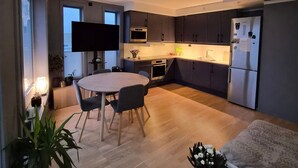Een moderne keuken met donkere kasten, een inbouwoven en een koelkast. Er is een eettafel met stoelen en een kamerplant.