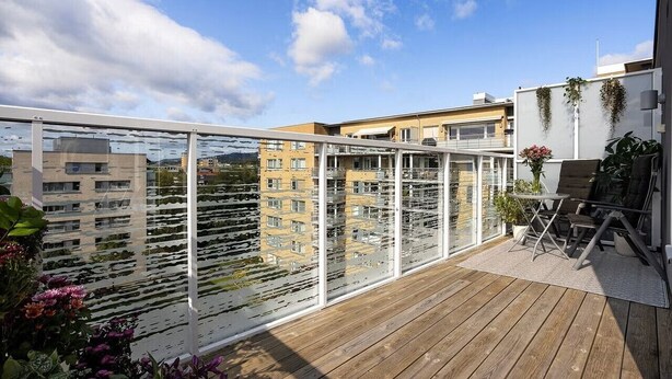Een houten terras met glazen balustrade, met uitzicht op een stadsbeeld.