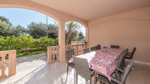 Un patio al aire libre con una mesa lista para comer, rodeado de sillas de mimbre y vistas a follaje y árboles.