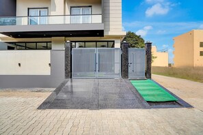 A modern two-story building with a gated entrance, paved driveway, and a green mat.