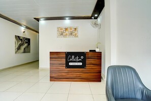 A reception area with a wooden reception desk, a blue leather chair, and two wall-mounted artworks. - Collection O Zeta I Noida (Greater Noida)