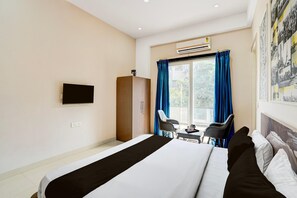 A hotel room with a bed, a desk with two chairs, a television on the wall, and a window with curtains. - Collection O Zeta I Noida (Greater Noida)