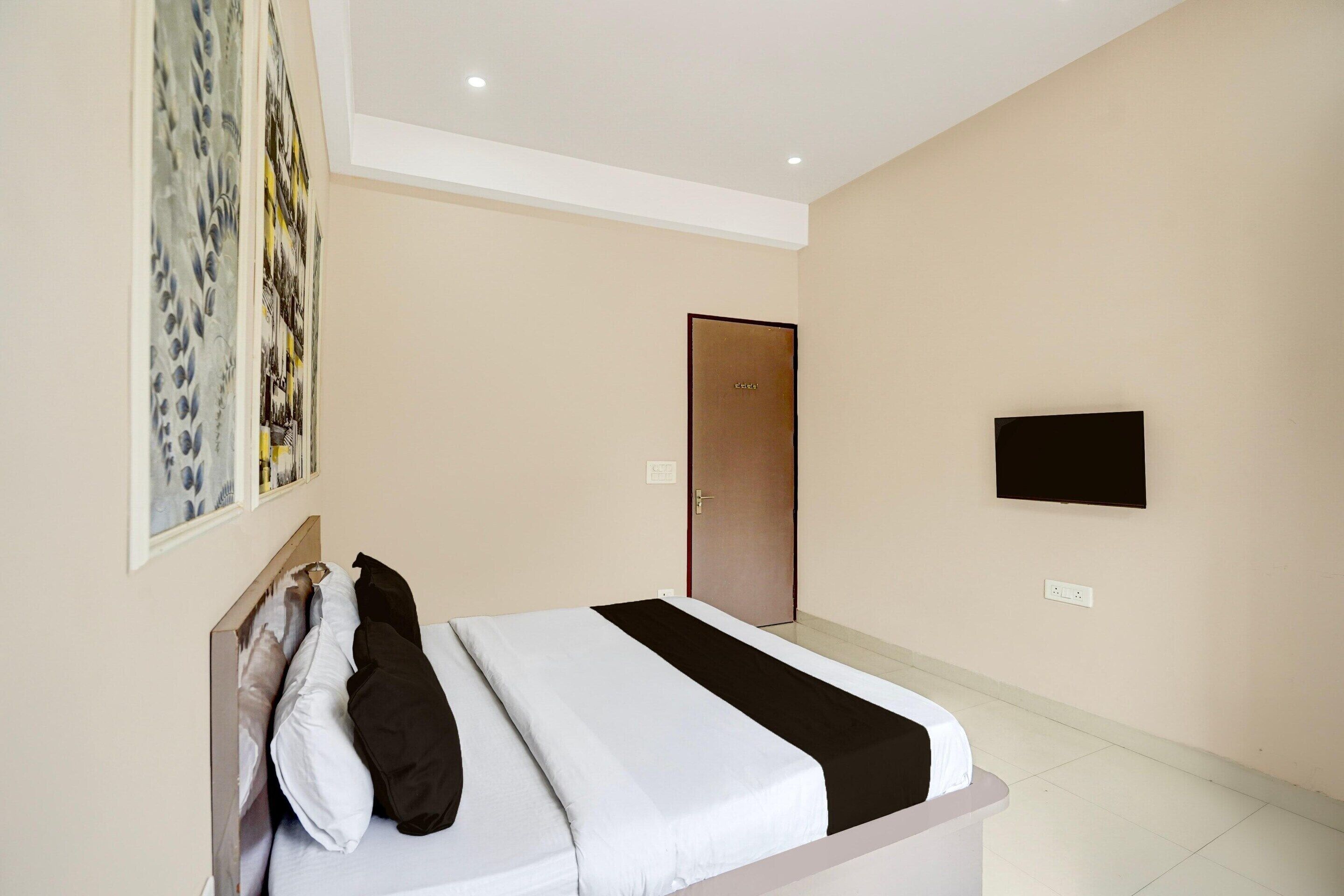A hotel room with a bed, a door, a flat-screen TV, and a wall-mounted artwork.