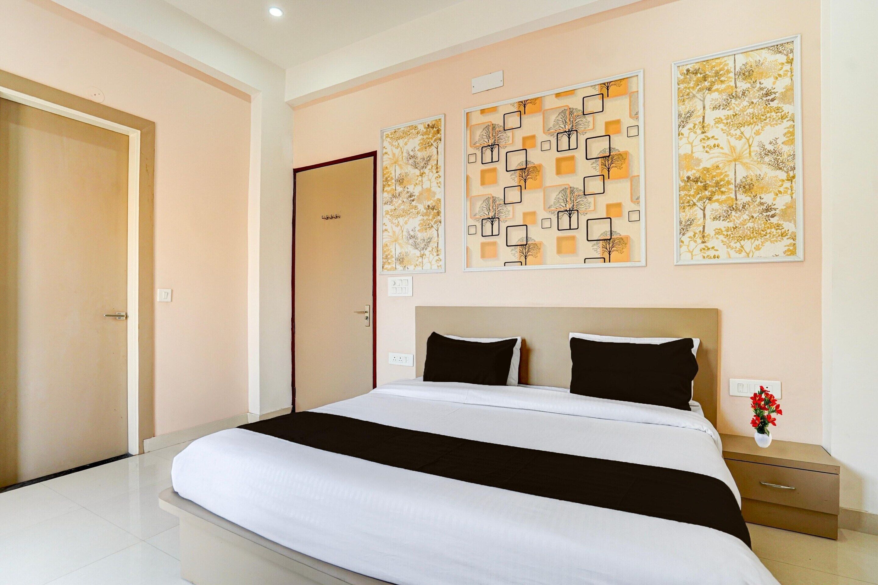 A hotel room with a large bed, a nightstand with a vase of flowers, and artwork on the walls.