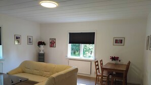 A living room with a beige sofa, a wooden dining table with chairs, a radiator, and a window with blinds. - Family-friendly Apartment Retreat in Dalarna Sweden (Orsa)