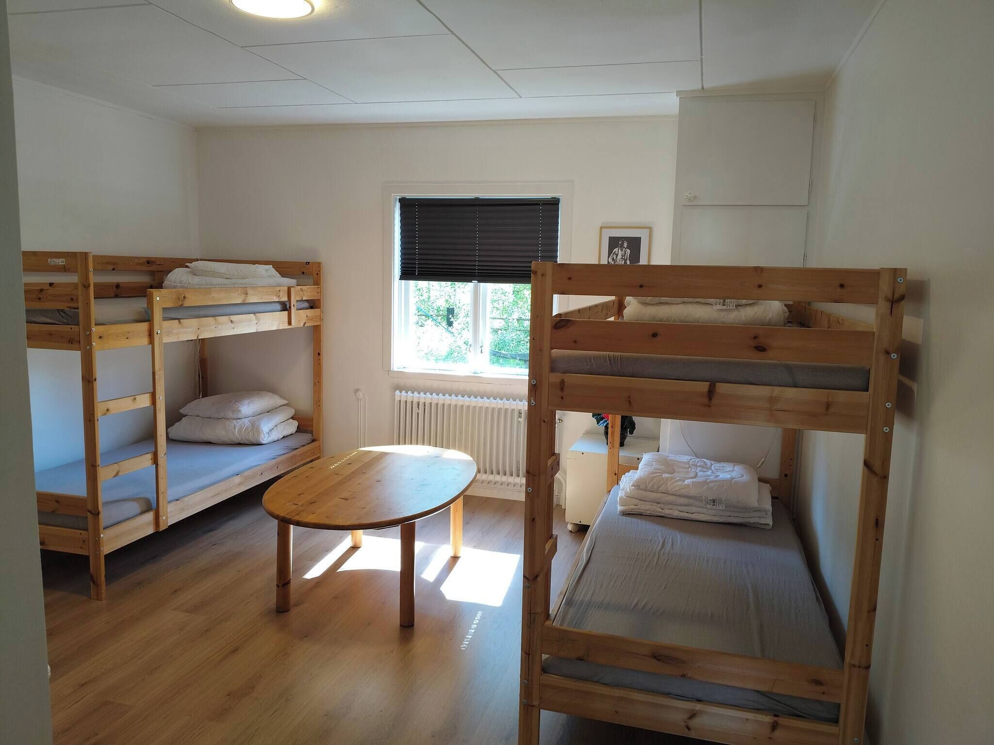 Een studentenkamer met stapelbedden, een klein tafeltje en een raam met jaloezieën.